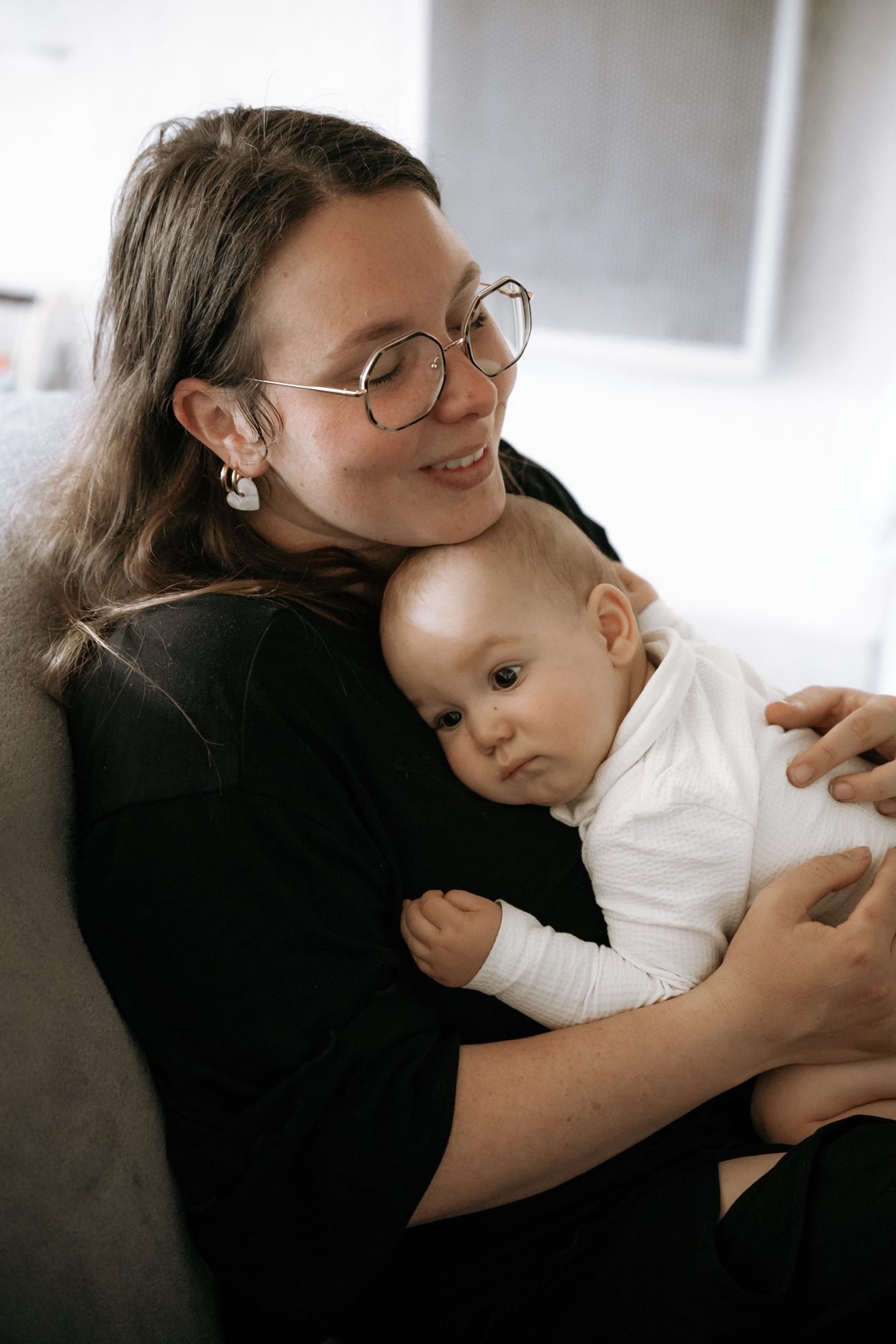 Maman en robe blanche tenant son bébé dans une ferme en pierre