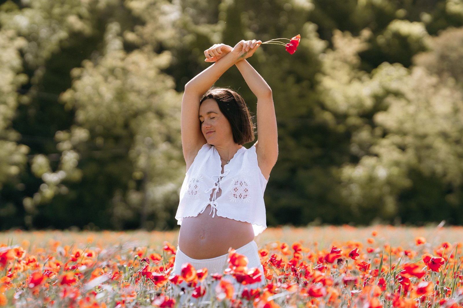 Femme enceinte bras levés tenant un coquelicot, champ de fleurs
