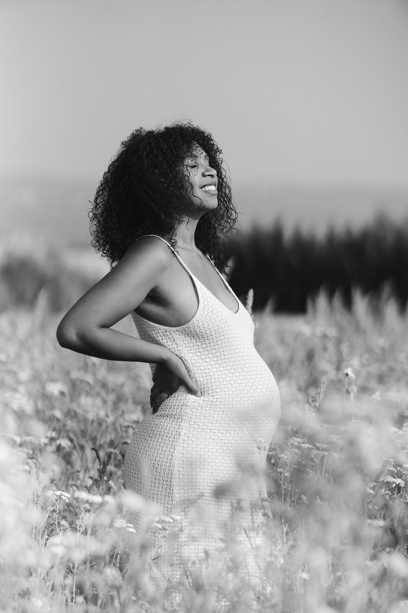 Femme enceinte en noir et blanc, de profil dans un champ de hautes herbes