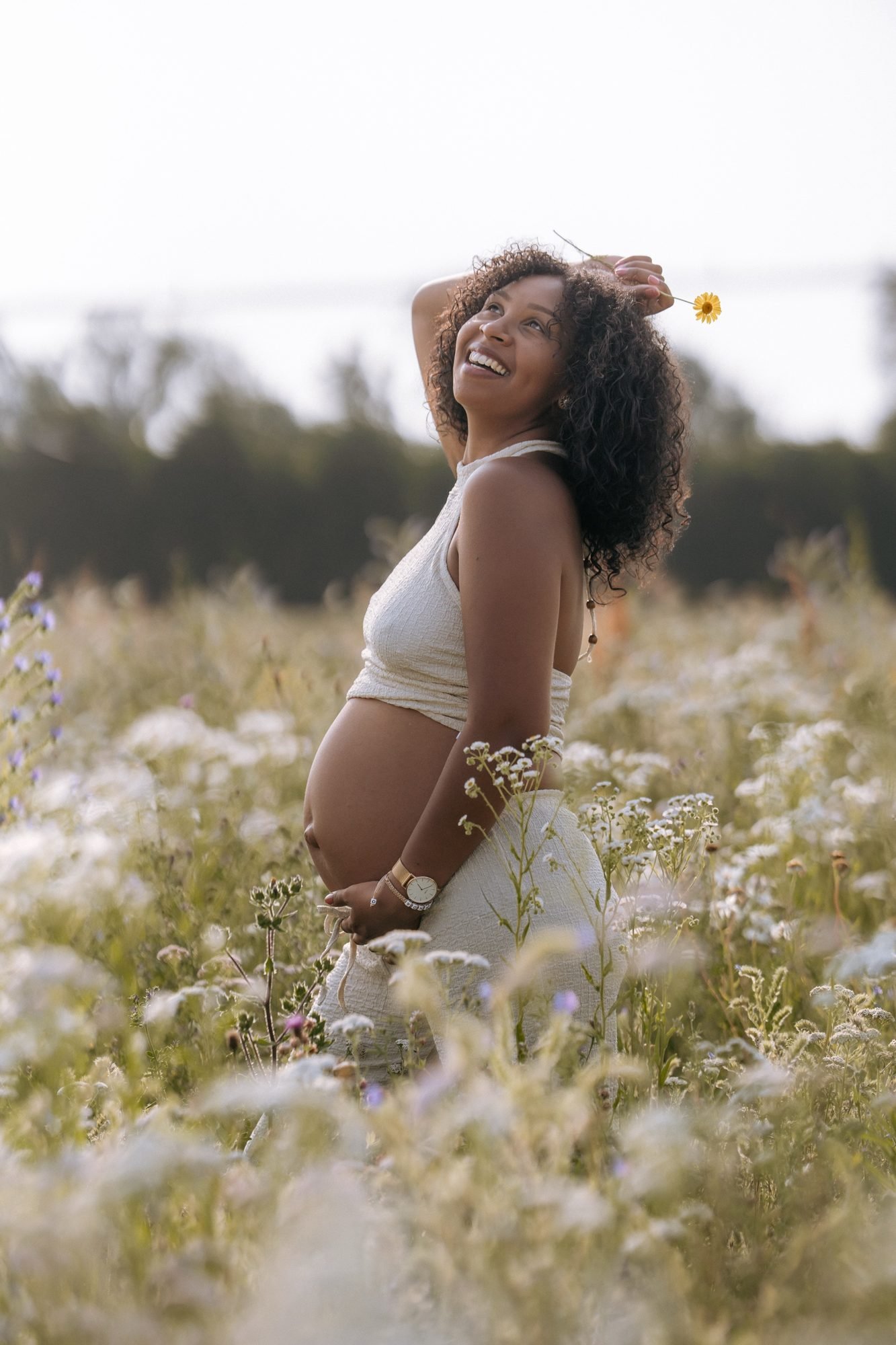 Femme enceinte souriante tenant une fleur jaune, champ de fleurs sauvages