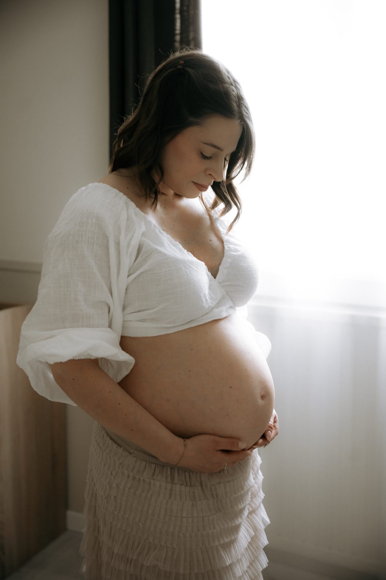 Ventre de femme enceinte, mains croisées, lumière du matin