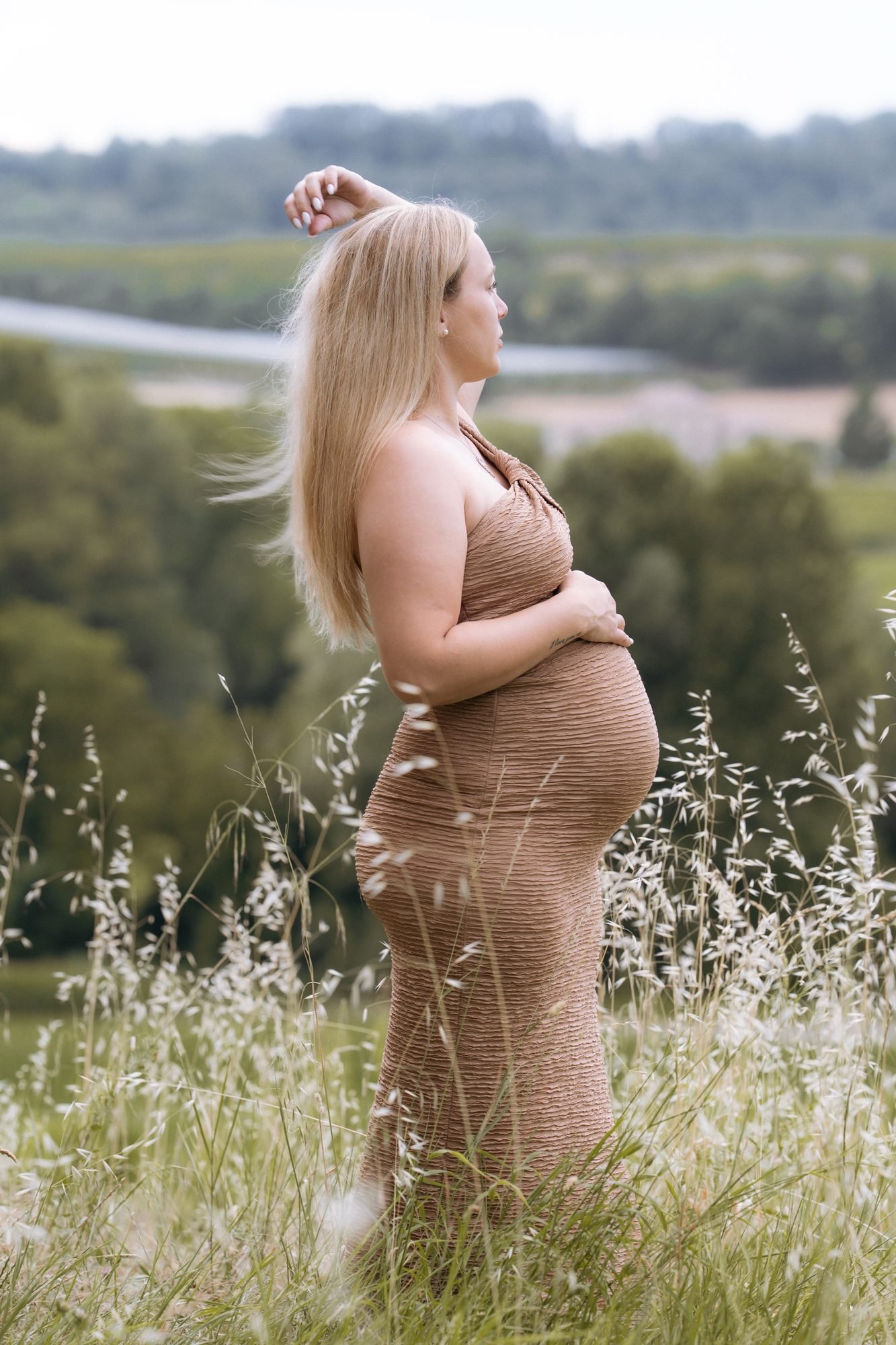 Femme enceinte de profil devant un paysage de campagne, robe beige