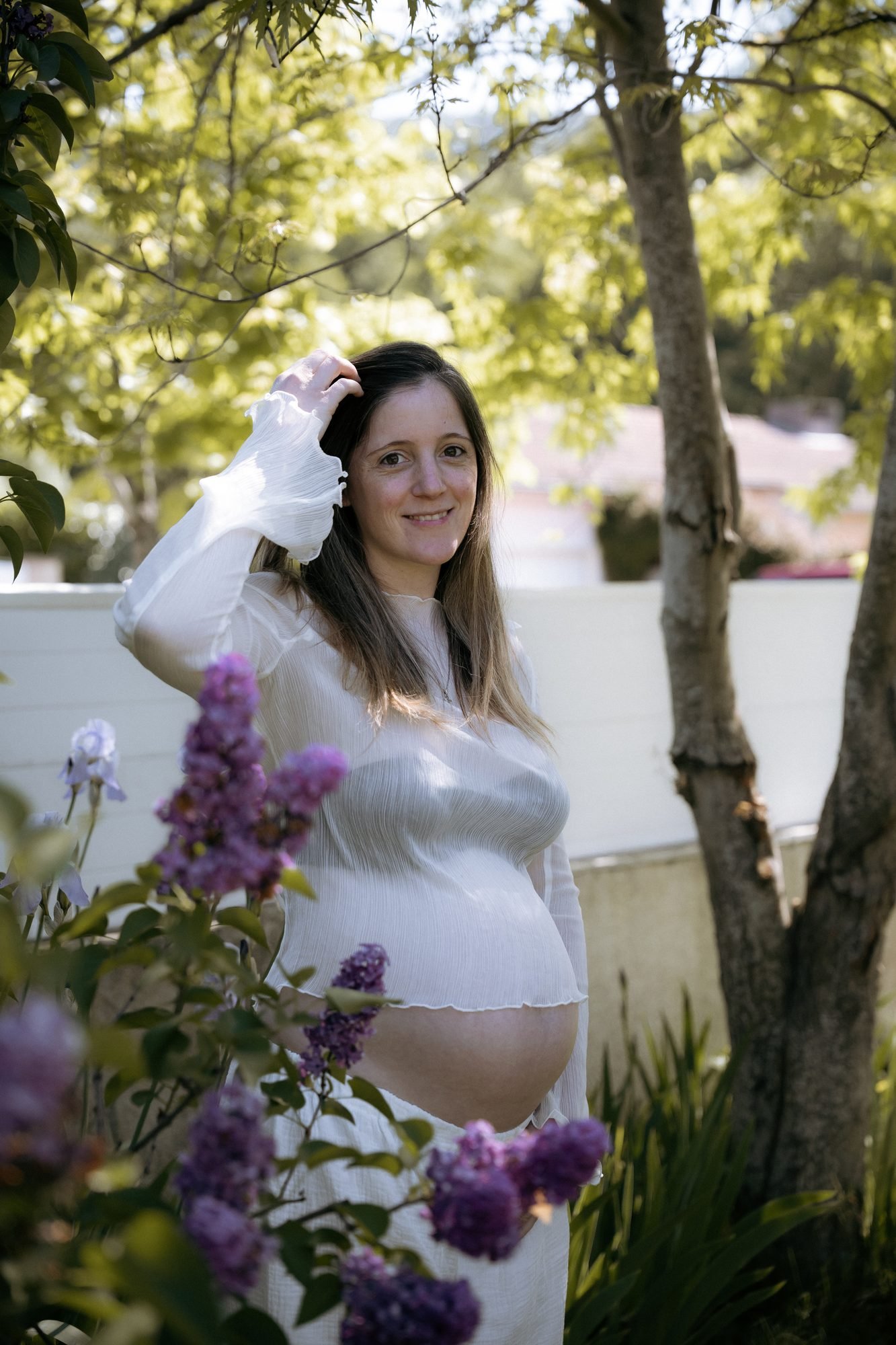 Femme enceinte souriante dans un jardin, main dans les cheveux