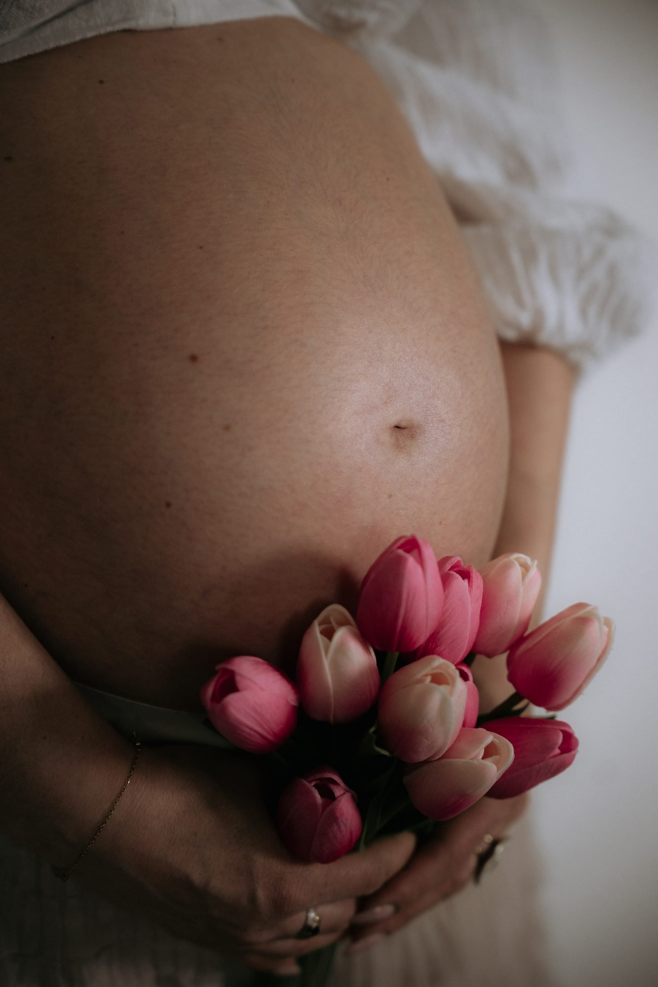 Ventre de femme enceinte tenant un bouquet de tulipes roses et blanches, tenue blanche légère