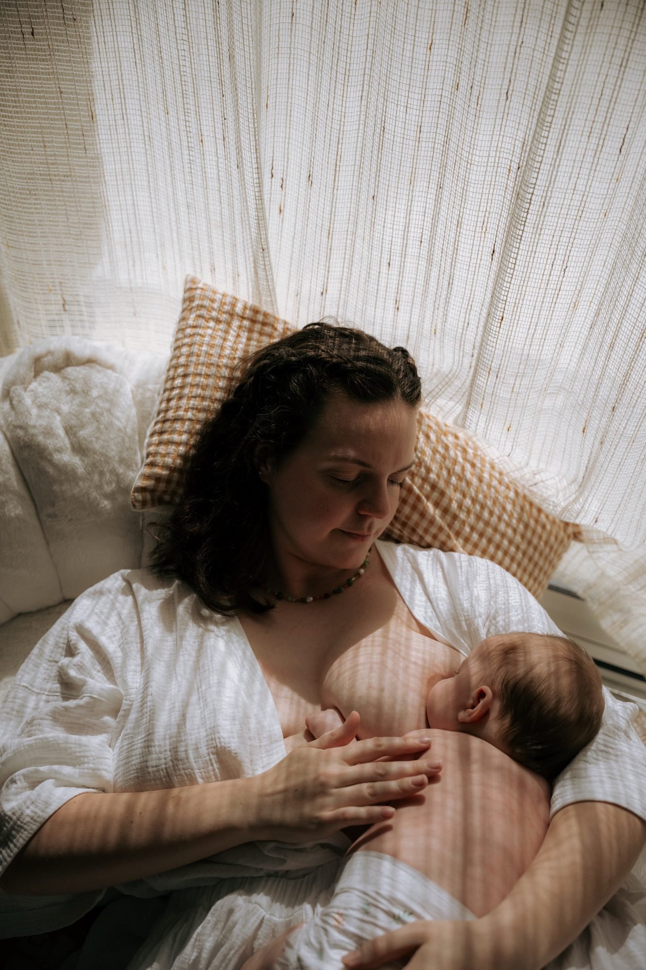 Mère allongée allaitant son nouveau-né, coussins et voilage