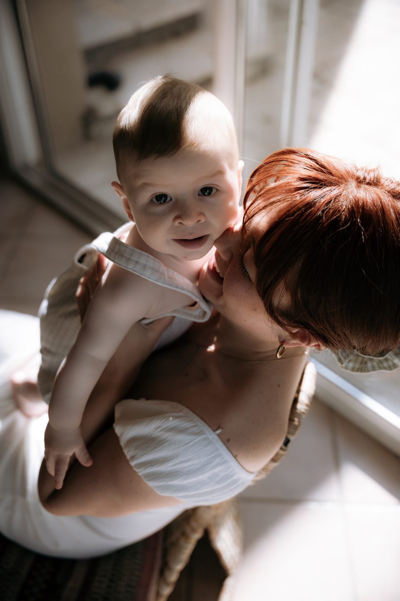 Mère aux cheveux roux cajolant son bébé près d'une fenêtre