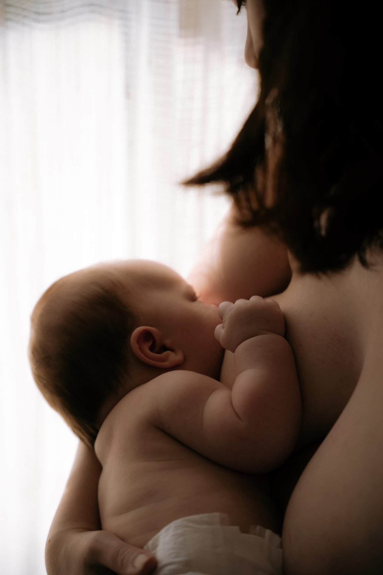 Mère allaitant son bébé près d'une fenêtre, lumière douce, bébé tenant la main de sa mère